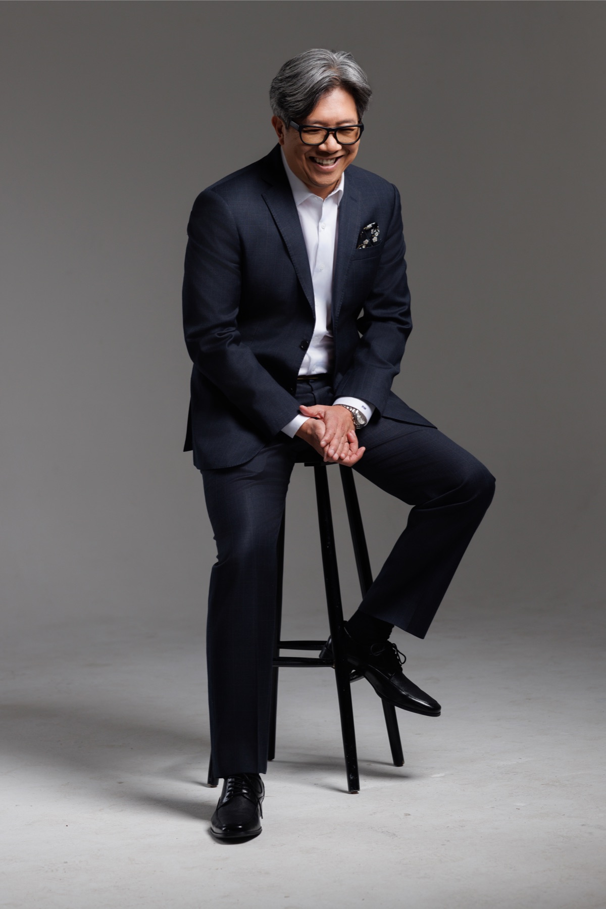 Rengie Mendoza, seated on a stool in a navy suit, laughing